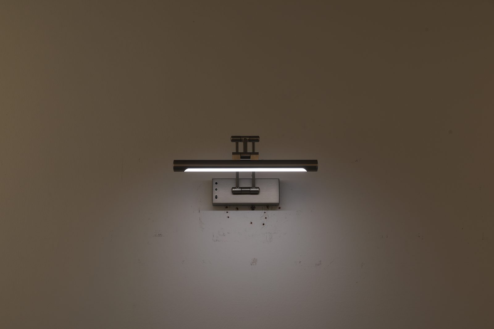 Spiegelleuchte in Nickel-Optik mit warmem Licht an grauer Wand